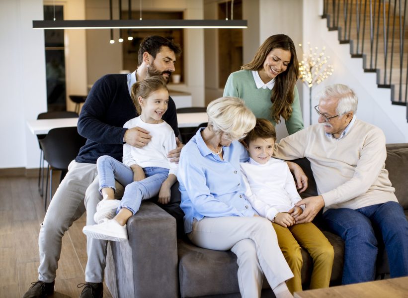 Multi generation family sitting together on the sofa at modern home and watching TV